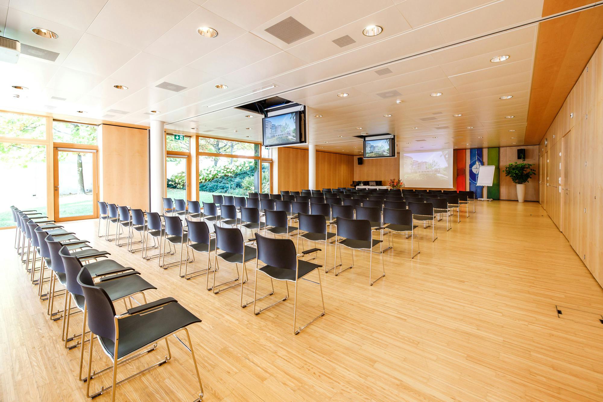 Leerer Konferenzraum mit Reihen von Stühlen und Präsentationstechnik.